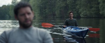 Movie still from “The Good Neighbor” (2022), directed by Stephan Rick – A man in a blue canoe with a red paddle; Medium shot, Over the shoulder angle