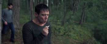 Movie still from “The Good Neighbor” (2022), directed by Stephan Rick – A man in the woods smoking a cigarette; Close Up shot, Over the shoulder angle