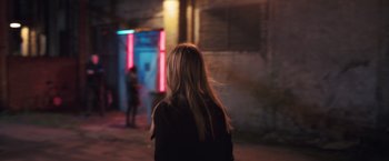 Movie still from “The Good Neighbor” (2022), directed by Stephan Rick – A woman standing on the side of the street at night; Medium shot, Over the shoulder angle