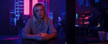Movie still from “The Good Neighbor” (2022), directed by Stephan Rick – A woman sitting at a table in a dark room; Medium shot, Over the shoulder angle
