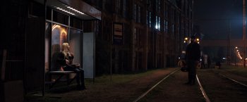 Movie still from “The Good Neighbor” (2022), directed by Stephan Rick – A man sitting on a bench in front of a building at night; Extreme Wide shot, Low angle