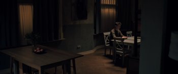 Movie still from “The Good Neighbor” (2022), directed by Stephan Rick – A man sitting at a table in a dark room; Wide shot, High angle