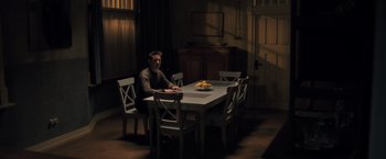 Movie still from “The Good Neighbor” (2022), directed by Stephan Rick – A man sitting at a dining room table with a bowl of fruit on the table; Wide shot, High angle