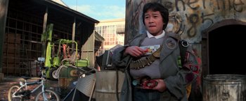 Movie still from “The Goonies” (1985), directed by Richard Donner – A person standing in front of a building holding a plate; Medium shot, Low angle