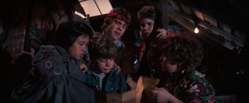 Movie still from “The Goonies” (1985), directed by Richard Donner – A group of young men looking at a paper bag; Medium shot, High angle