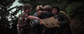 Movie still from “The Goonies” (1985), directed by Richard Donner – A group of young people standing next to each other on a field; Medium shot, High angle