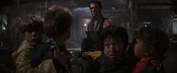 Movie still from “The Goonies” (1985), directed by Richard Donner – A group of young people standing next to each other in a room; Medium shot, Over the shoulder angle