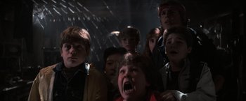 Movie still from “The Goonies” (1985), directed by Richard Donner – A group of children are watching something in the dark; Medium shot, Low angle