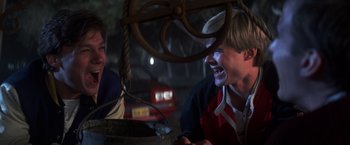 Movie still from “The Goonies” (1985), directed by Richard Donner – Two young men laugh while sitting on a swing; Medium shot, Low angle