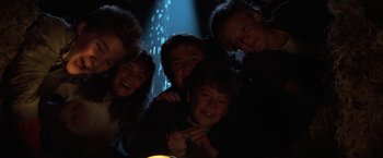 Movie still from “The Goonies” (1985), directed by Richard Donner – A group of people posing for a picture in the dark; Medium shot, Low angle