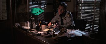 Movie still from “The Goonies” (1985), directed by Richard Donner – A man sitting at a table with a green hat on; Medium shot, High angle
