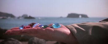 Movie still from “The Goonies” (1985), directed by Richard Donner – A hand holding a blue and green glass object; Extreme Close Up shot, Over the shoulder angle