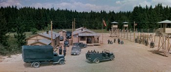 Movie still from “The Great Escape” (1963), directed by John Sturges – A group of men standing next to each other in front of a building; Extreme Wide shot, High angle