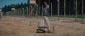 Movie still from “The Great Escape” (1963), directed by John Sturges – A man walking with a duffel bag in a dirt field; Wide shot, Low angle