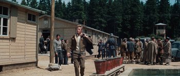 Movie still from “The Great Escape” (1963), directed by John Sturges – A group of people standing around a building; Wide shot, Over the shoulder angle