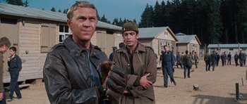 Movie still from “The Great Escape” (1963), directed by John Sturges – A man holding a baseball glove next to another man in a uniform; Medium shot, Over the shoulder angle