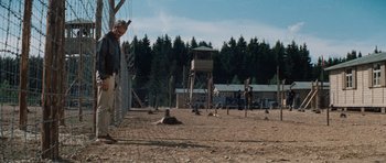 Movie still from “The Great Escape” (1963), directed by John Sturges – A man standing next to a fence in the dirt; Wide shot, Over the shoulder angle