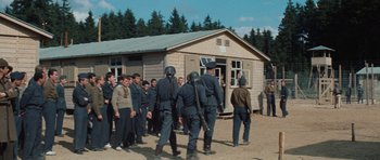 Movie still from “The Great Escape” (1963), directed by John Sturges – A group of men standing in front of a wooden building; Wide shot, High angle