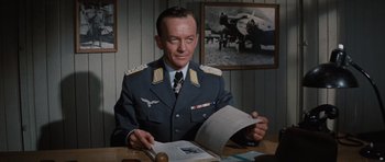 Movie still from “The Great Escape” (1963), directed by John Sturges – A man sitting at a table with papers in front of him; Medium shot, Low angle