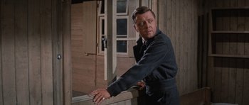 Movie still from “The Great Escape” (1963), directed by John Sturges – A man leaning on a wooden railing near a building; Medium shot, Over the shoulder angle