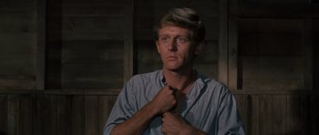 Movie still from “The Great Escape” (1963), directed by John Sturges – A man adjusts his neck tie in front of a wooden wall; Close Up shot, Low angle