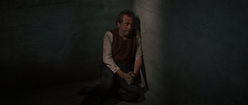 Movie still from “The Great Escape” (1963), directed by John Sturges – A man sitting on the ground with his hands crossed; Medium shot, High angle