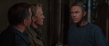 Movie still from “The Great Escape” (1963), directed by John Sturges – Two men standing next to each other in front of a brick wall; Close Up shot, Over the shoulder angle
