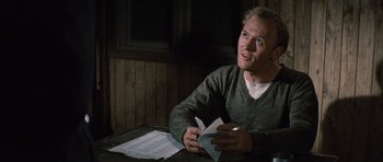 Movie still from “The Great Escape” (1963), directed by John Sturges – A man sitting at a table with papers in front of him; Medium shot, Over the shoulder angle