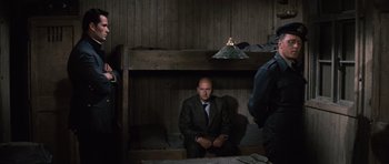 Movie still from “The Great Escape” (1963), directed by John Sturges – A man in a suit and tie sitting on a bunk bed; Wide shot, Over the shoulder angle