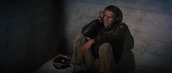 Movie still from “The Great Escape” (1963), directed by John Sturges – A man sitting on the ground with a baseball glove in front of him; Medium shot, High angle