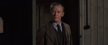 Movie still from “The Great Escape” (1963), directed by John Sturges – A man wearing a suit and tie standing in a room; Close Up shot, Low angle
