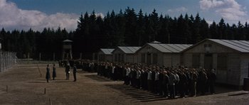 Movie still from “The Great Escape” (1963), directed by John Sturges – A large group of people standing in front of a row of houses; Extreme Wide shot, High angle