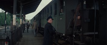 Movie still from “The Great Escape” (1963), directed by John Sturges – A man in a hat standing in front of a train; Wide shot, Over the shoulder angle