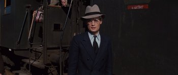 Movie still from “The Great Escape” (1963), directed by John Sturges – A man in a suit and hat standing in front of a camera; Medium shot, Over the shoulder angle