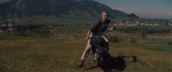 Movie still from “The Great Escape” (1963), directed by John Sturges – A man riding a motorcycle on top of a grass covered field; Wide shot, Low angle