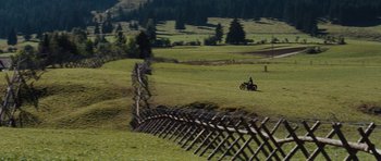 Movie still from “The Great Escape” (1963), directed by John Sturges – A person riding a motorcycle on top of a grass covered field; Extreme Wide shot, High angle