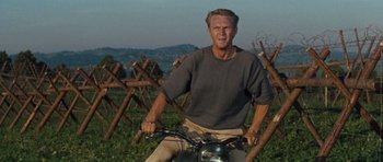 Movie still from “The Great Escape” (1963), directed by John Sturges – A man riding a motorcycle on top of a grass covered field; Medium shot, Low angle