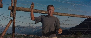 Movie still from “The Great Escape” (1963), directed by John Sturges – A man in a grey shirt is holding up a peace sign; Medium shot, Low angle