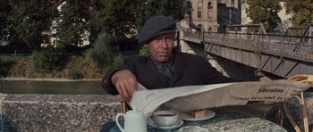 Movie still from “The Great Escape” (1963), directed by John Sturges – A man sitting at a table holding a newspaper; Medium shot, High angle