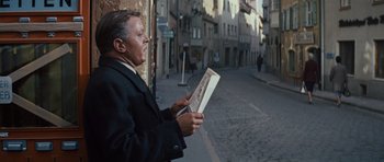 Movie still from “The Great Escape” (1963), directed by John Sturges – A man standing on the side of the street holding a newspaper; Medium shot, Over the shoulder angle
