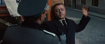 Movie still from “The Great Escape” (1963), directed by John Sturges – A man in a suit and tie standing next to another man in a suit; Medium shot, Over the shoulder angle