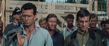 Movie still from “The Great Escape” (1963), directed by John Sturges – A group of men standing next to each other in front of a fence; Medium shot, Low angle