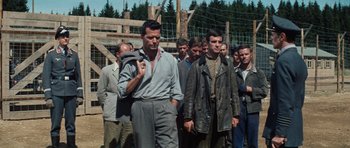 Movie still from “The Great Escape” (1963), directed by John Sturges – A group of men standing next to each other in front of barbed wire fence; Medium shot, Low angle