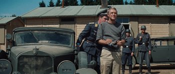 Movie still from “The Great Escape” (1963), directed by John Sturges – A man standing in front of an old car; Medium shot, Low angle