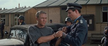 Movie still from “The Great Escape” (1963), directed by John Sturges – A man in a grey shirt and a man in a blue uniform; Medium shot, Over the shoulder angle