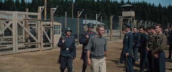 Movie still from “The Great Escape” (1963), directed by John Sturges – A group of men standing next to each other on top of a dirt field; Wide shot, Low angle
