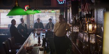 Movie still from “The Greatest Beer Run Ever” (2022), directed by Peter Farrelly – A man standing in front of a bar with two other men sitting at the bar behind him; Wide shot, Over the shoulder angle