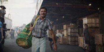 Movie still from “The Greatest Beer Run Ever” (2022), directed by Peter Farrelly – A man walking in a warehouse holding a green bag; Medium shot, Low angle