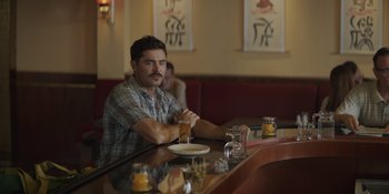 Movie still from “The Greatest Beer Run Ever” (2022), directed by Peter Farrelly – A man sitting at a table with a glass of beer; Medium shot, Over the shoulder angle