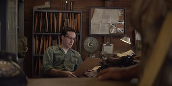 Movie still from “The Greatest Beer Run Ever” (2022), directed by Peter Farrelly – A man sitting at a table with a book in front of him; Medium shot, Over the shoulder angle